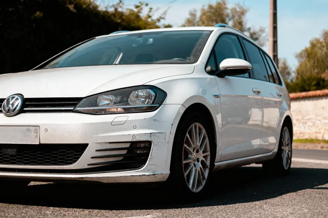 Voiture Volkswagen blanche garée sur route, lumière du jour, éraflures sur le pare-chocs avant.