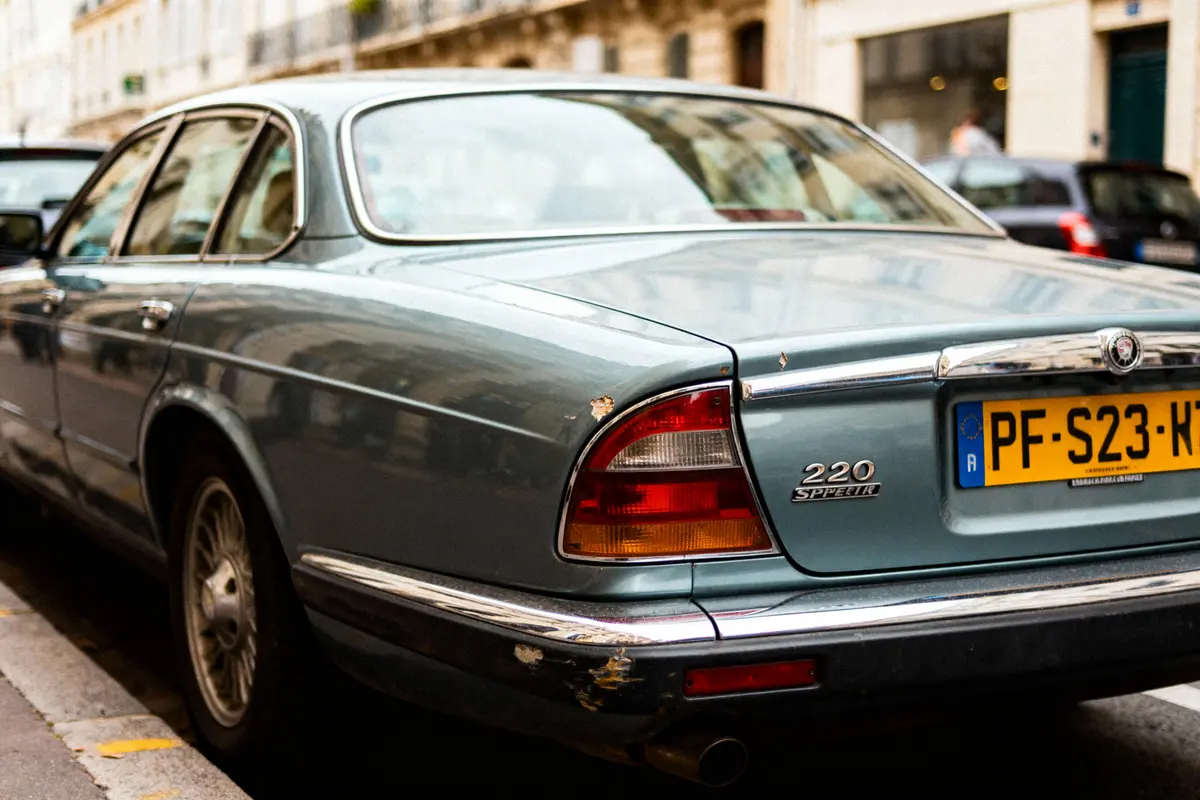 Voiture classique bleue stationnée, logo "220 Speeder", plaque française visible, rue urbaine à l'arrière-plan.