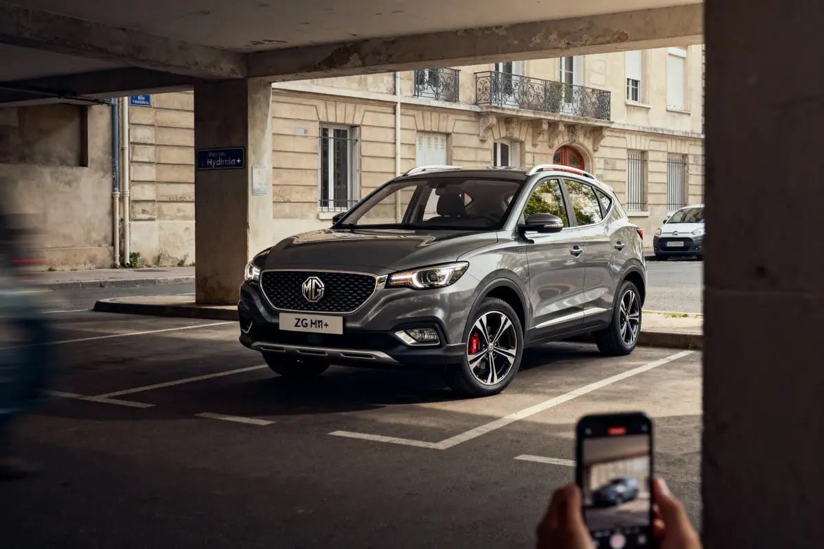 SUV gris stationné sous abri, photo prise avec un smartphone, bâtiment en pierre en arrière-plan.