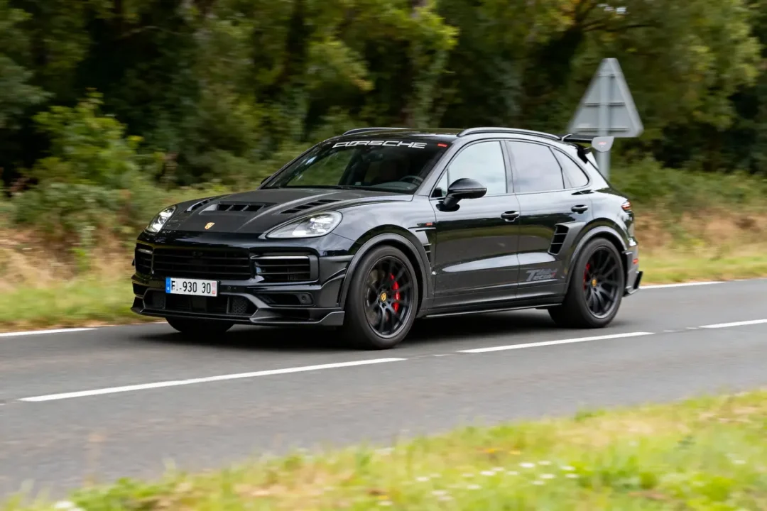 SUV noir Porsche roulant sur route, entouré de végétation. Voiture sportive et dynamique en mouvement.