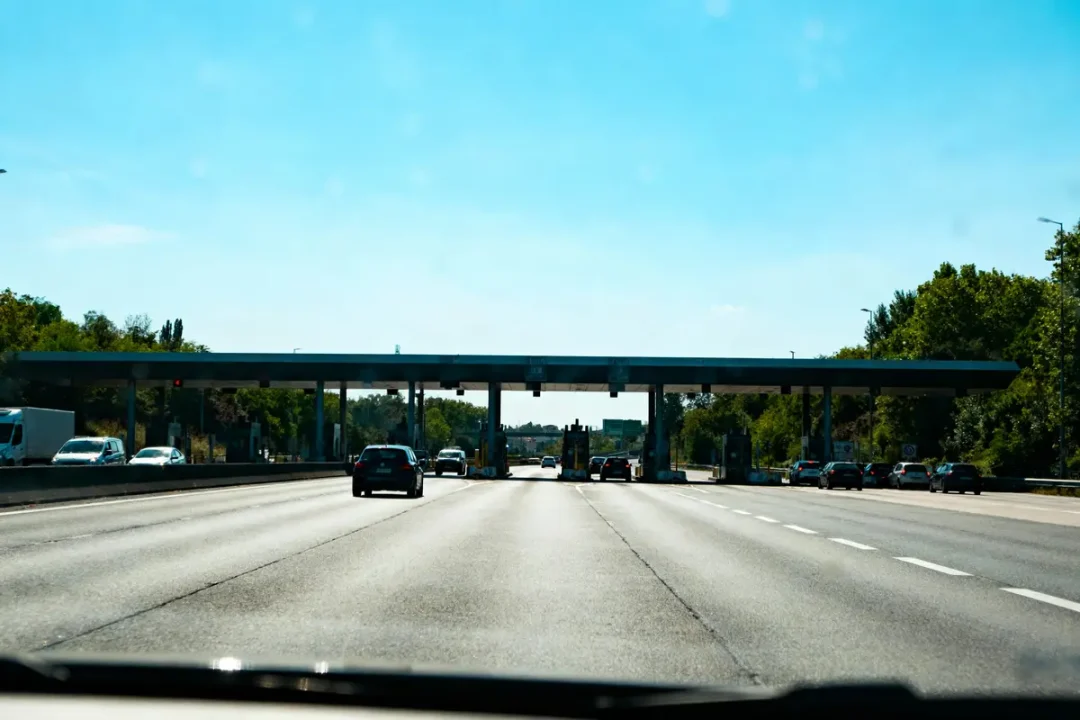 Autoroute avec voitures approchant une barrière de péage sous un ciel bleu.