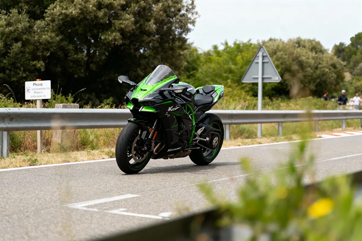 Moto verte et noire sur une route, bordée d'arbres et de panneaux routiers, ciel clair.