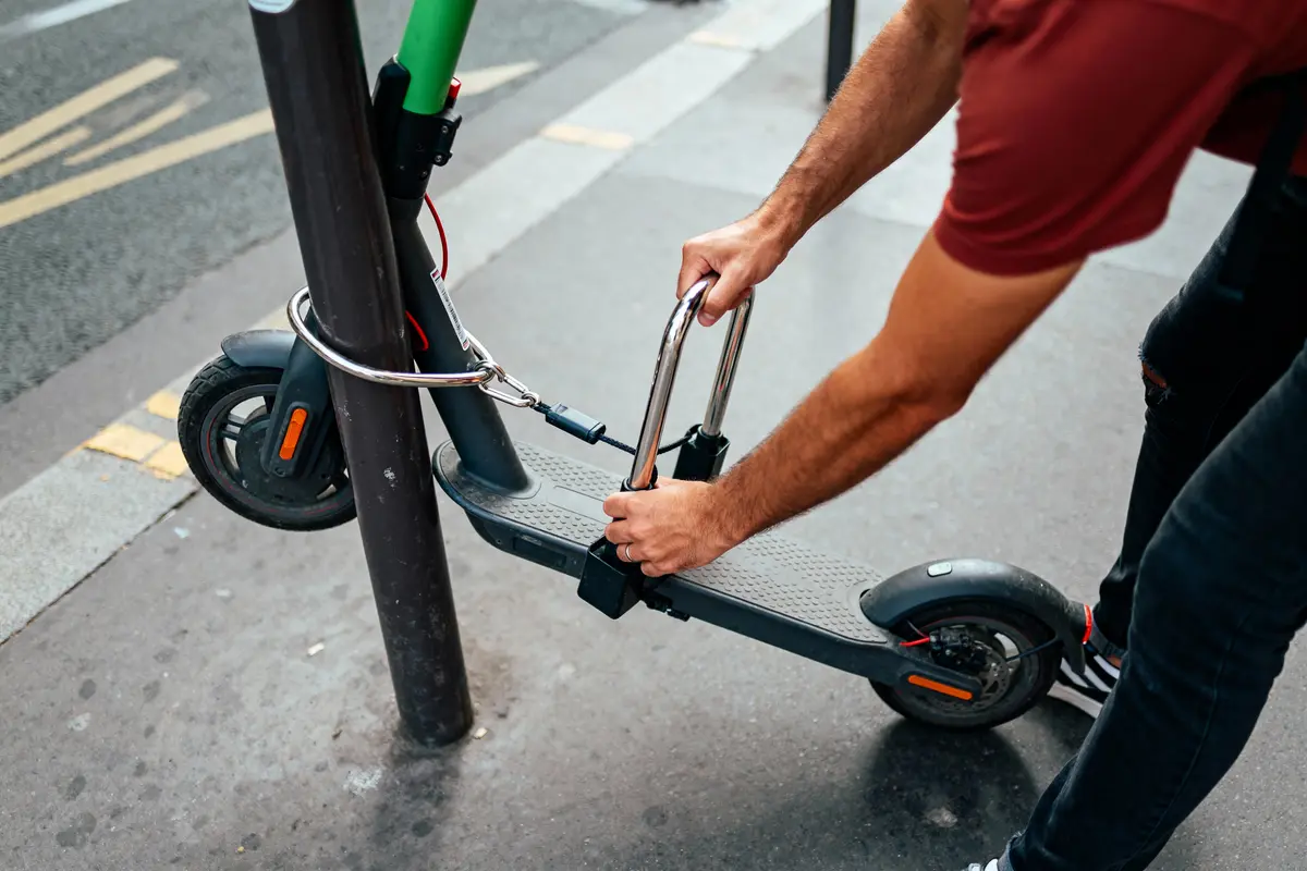 Personne verrouillant une trottinette électrique à un poteau avec un antivol en U.