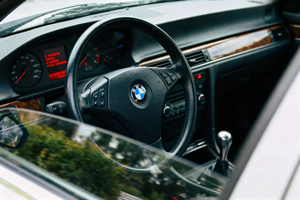 Volant et tableau de bord d’une voiture BMW, avec levier de vitesse, affichage numérique et finitions en bois.