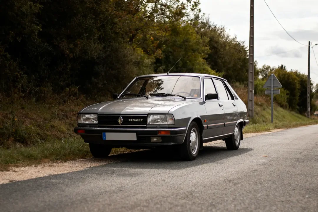 Voiture grise Renault sur route de campagne, arbres en arrière-plan, panneau de signalisation visible.