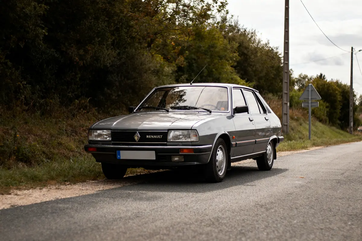 Voiture grise Renault sur route de campagne, arbres en arrière-plan, panneau de signalisation visible.