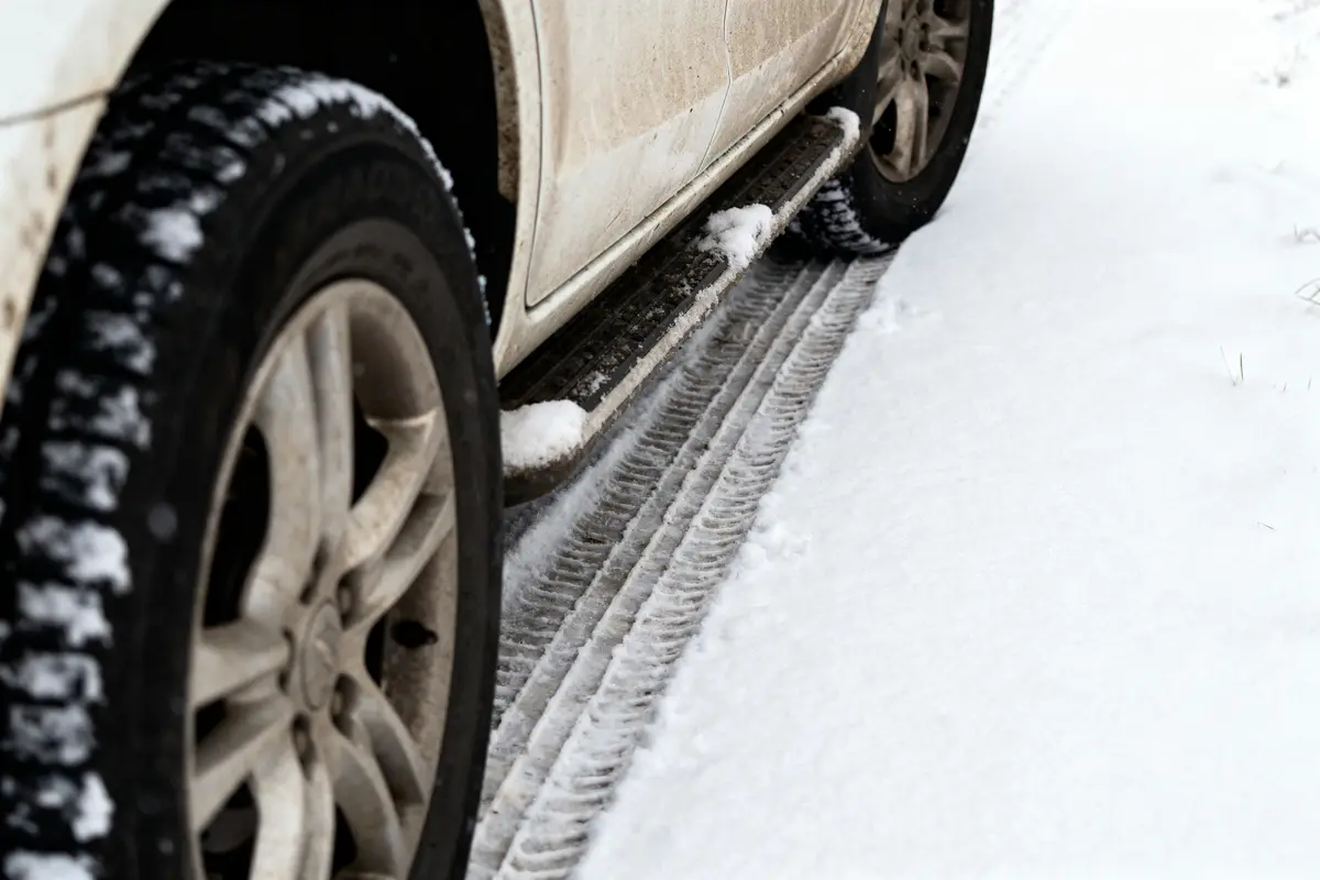 Pneus de voiture, traces sur route enneigée, voiture blanche. Neige et boue visibles sur le véhicule.