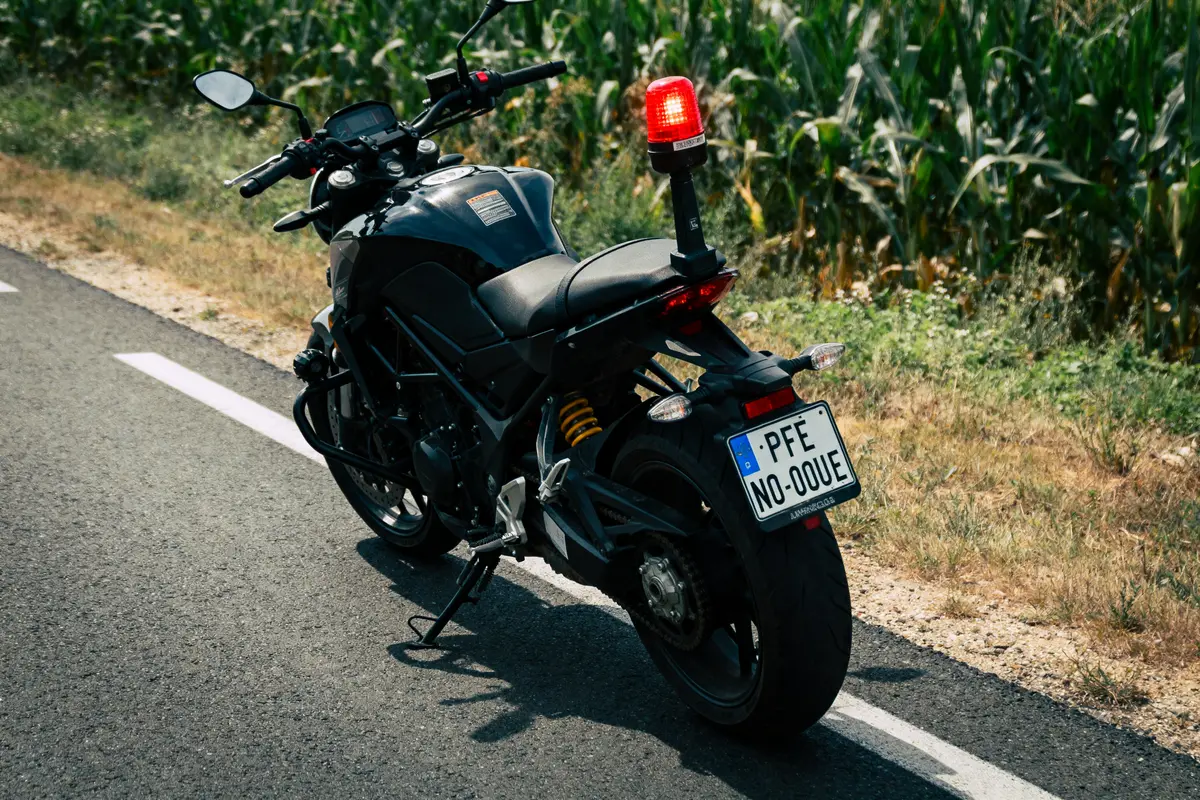 Moto noire garée sur route devant champ, gyrophare rouge allumé, par temps ensoleillé.