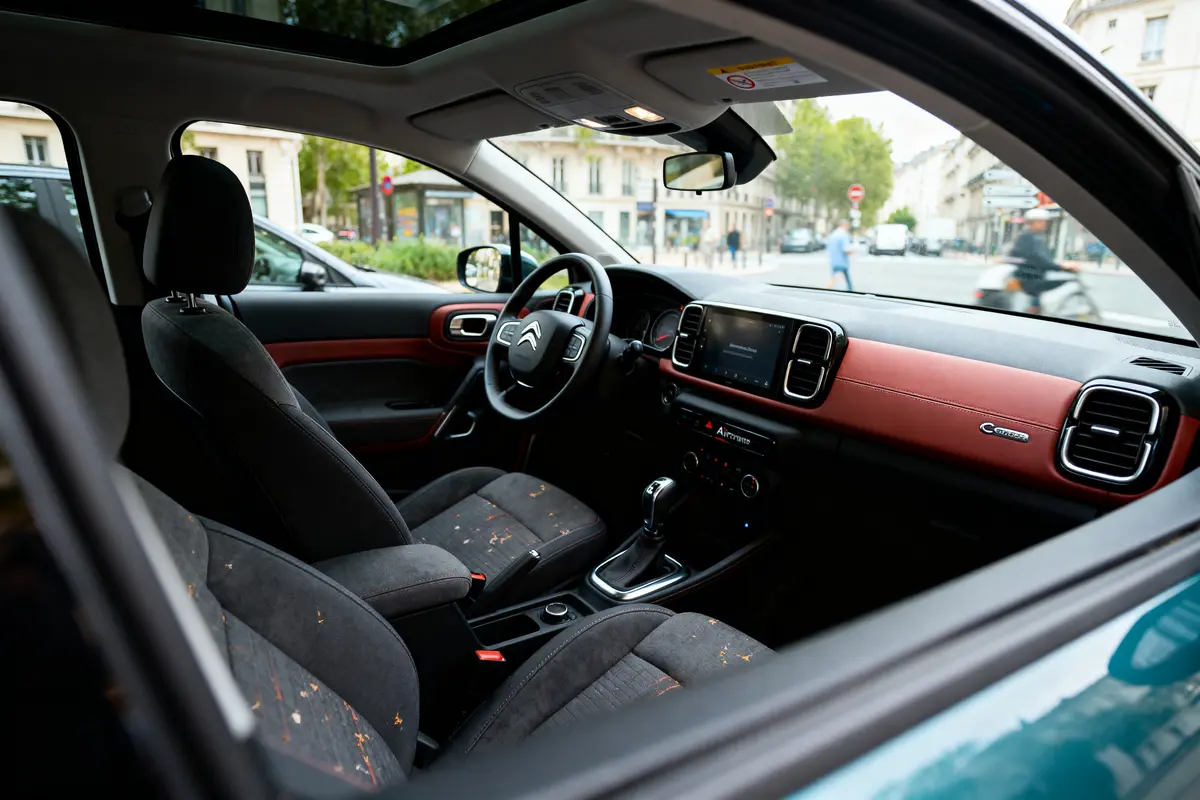 Intérieur d'une voiture Citroën moderne, vue avant, tableau de bord rouge, rue urbaine en arrière-plan.