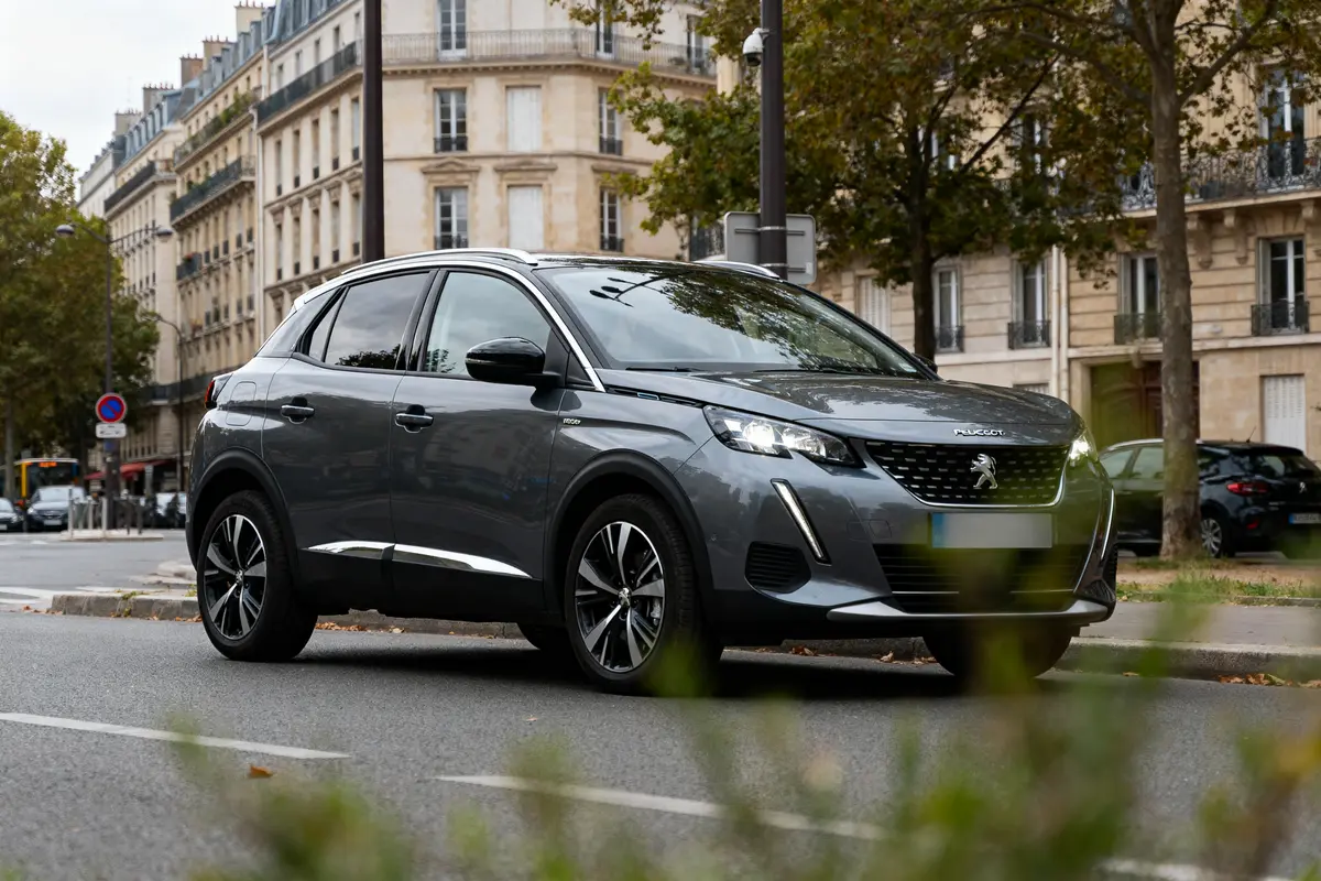 SUV Peugeot gris stationné sur une rue urbaine, bâtiments en arrière-plan, arbres et feuillage autour.