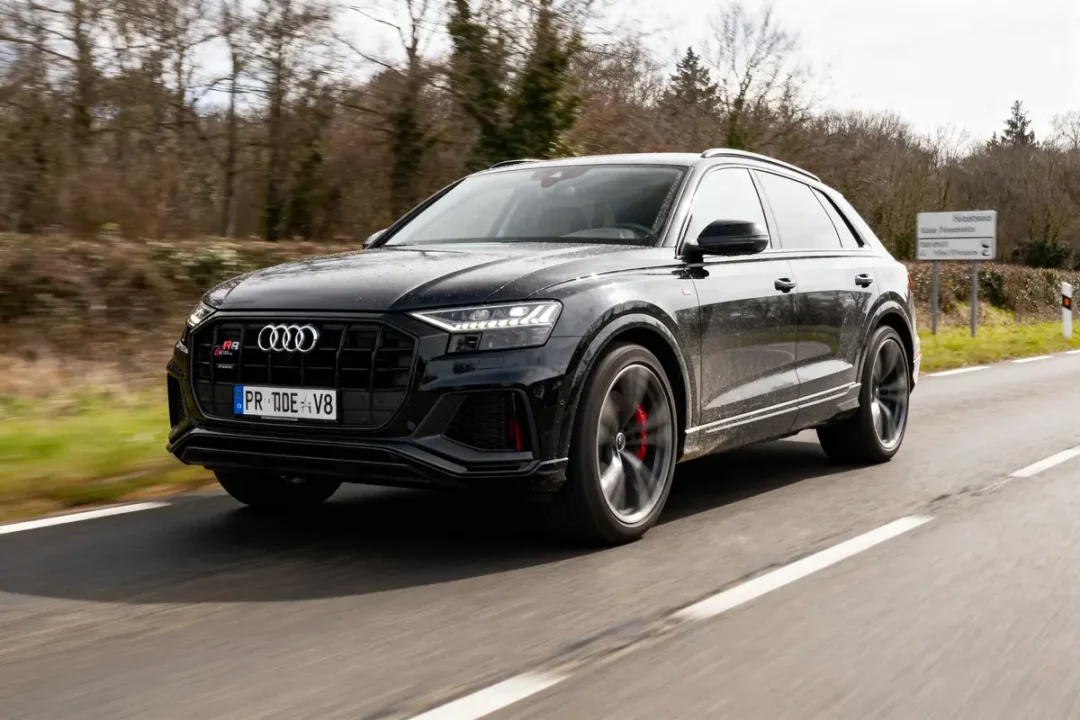 SUV Audi noir en mouvement sur route, arrière-plan forestier. Voiture moderne élégante et dynamique, plaque d'immatriculation visible.