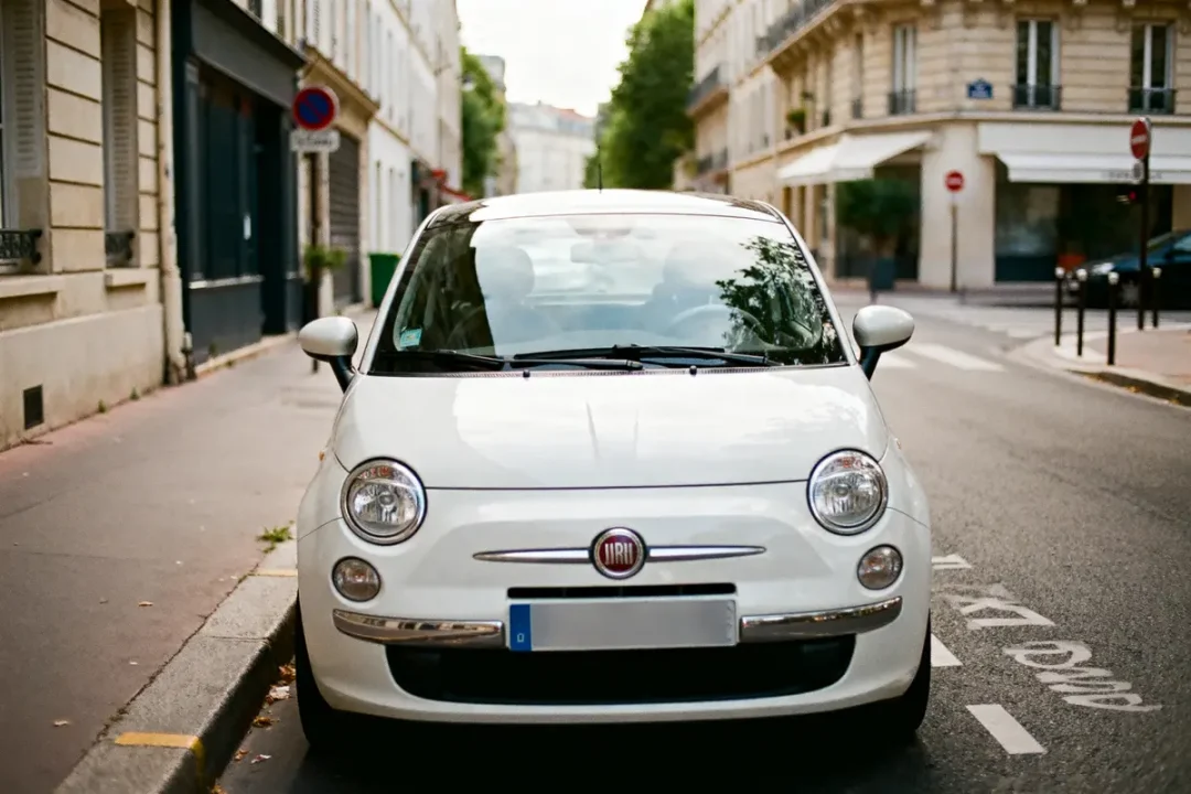 Voiture urbaine blanche garée dans une rue calme, bâtiments en arrière-plan.