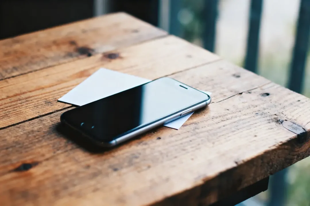 Smartphone noir sur table en bois rustique, avec papier blanc en arrière-plan flou.