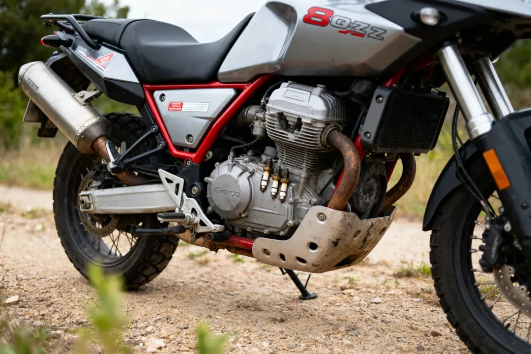 Moto grise et noire, modèle 8QZZ, sur chemin de terre, vue latérale du moteur et échappement.