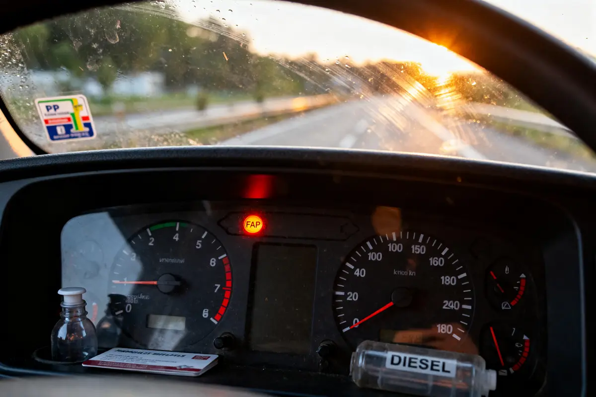 Tableau de bord de voiture au coucher du soleil, voyant FAP allumé, mélangeur diesel visible.