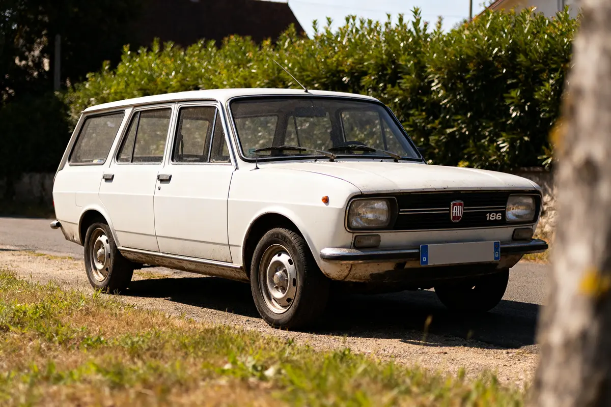 Vieille Fiat 128 Station Wagon blanche garée près d’une haie verdoyante en journée