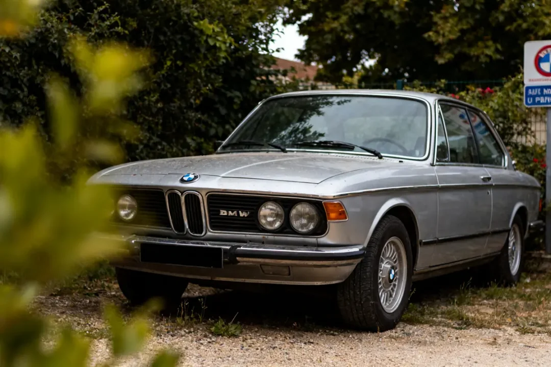 BMW ancienne grise stationnée sur un chemin bordé de végétation verte
