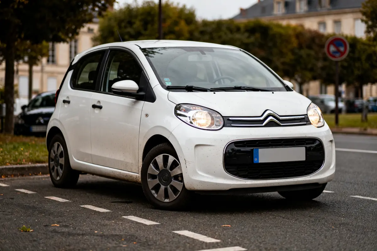 Citroen C1 blanche garée en ville sur une route bordée d'arbres
