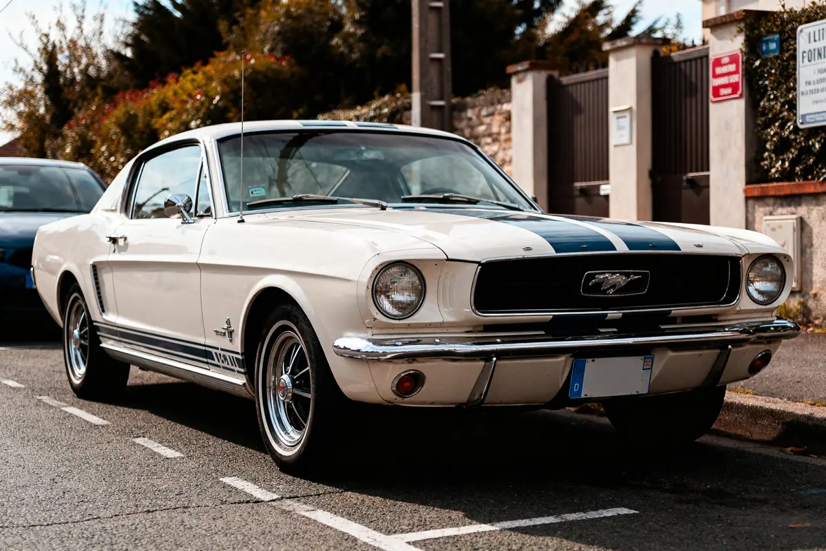 Ford Mustang 1967 blanche stationnée en rue devant portail en arrière-plan