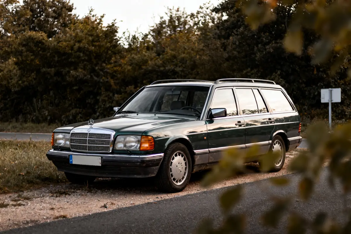 Voiture S124 Mercedes Benz verte garée en bord de route devant arbres