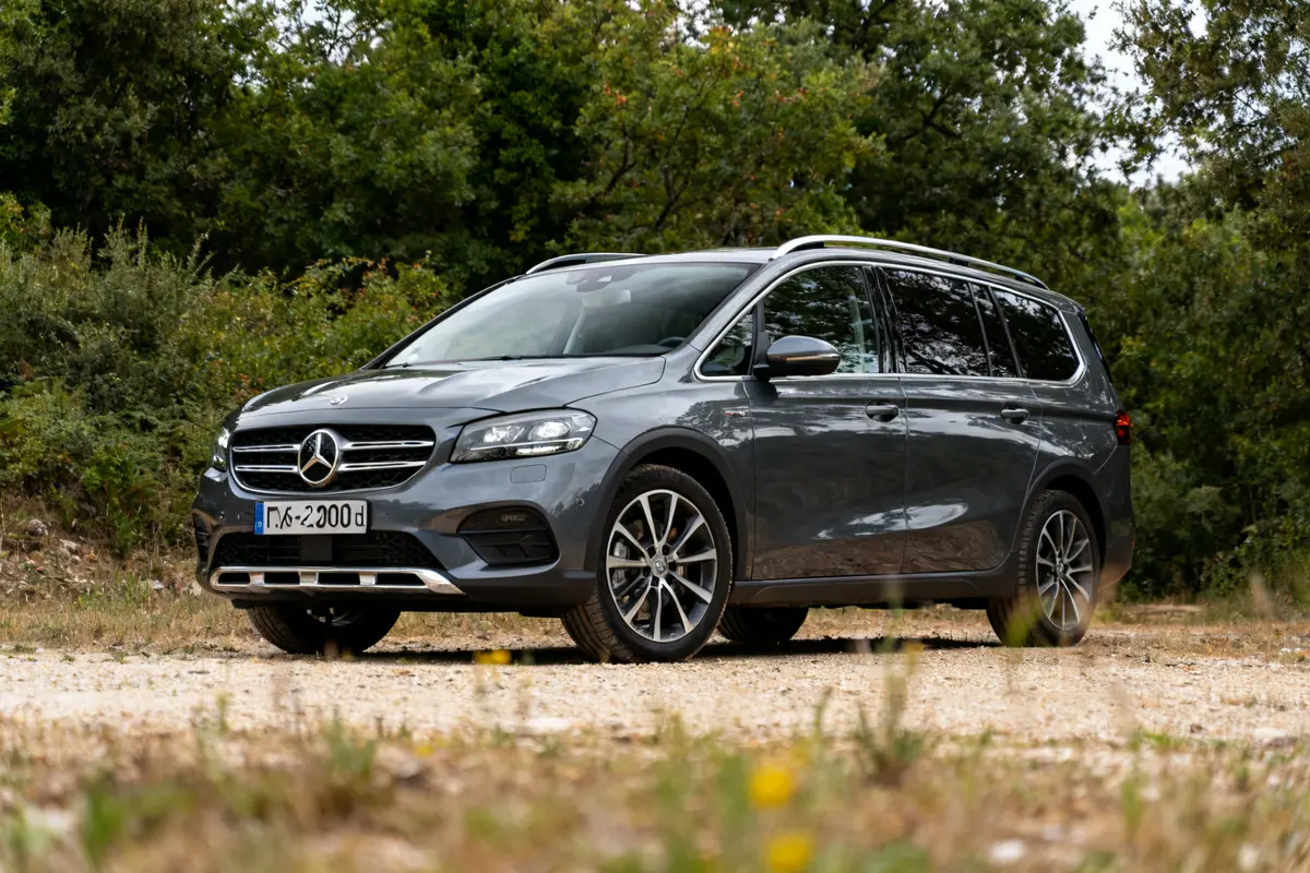 Voiture 7 places Mercedes gris foncé, garée en nature devant des arbres