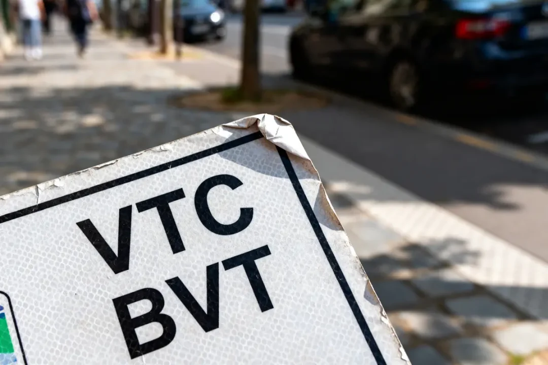 Panneau VTC BVT sur trottoir pavé, voitures floues en arrière-plan.