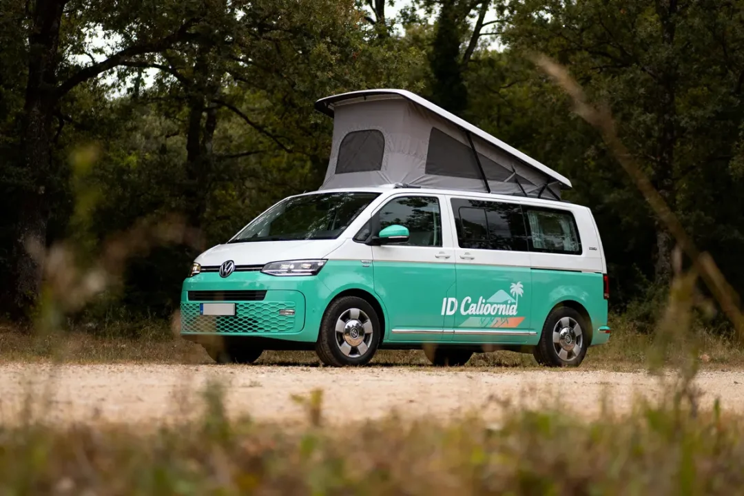 Fourgon aménagé Volkswagen ID California, vert et blanc, avec toit relevable, stationné dans une clairière boisée.