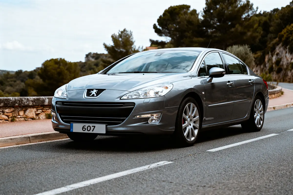Berline grise Peugeot 607 conduite sur route sinueuse, entourée d'arbres et de paysages naturels.