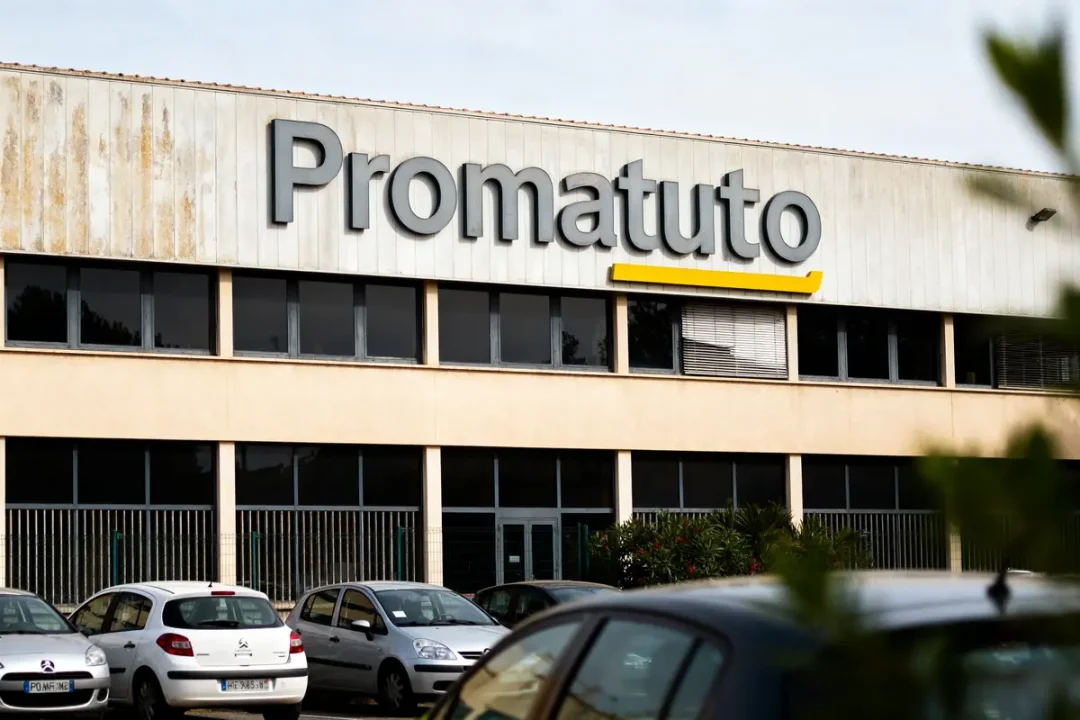 Bâtiment Promatuto avec des voitures garées devant, façade blanche et logo gris et jaune.