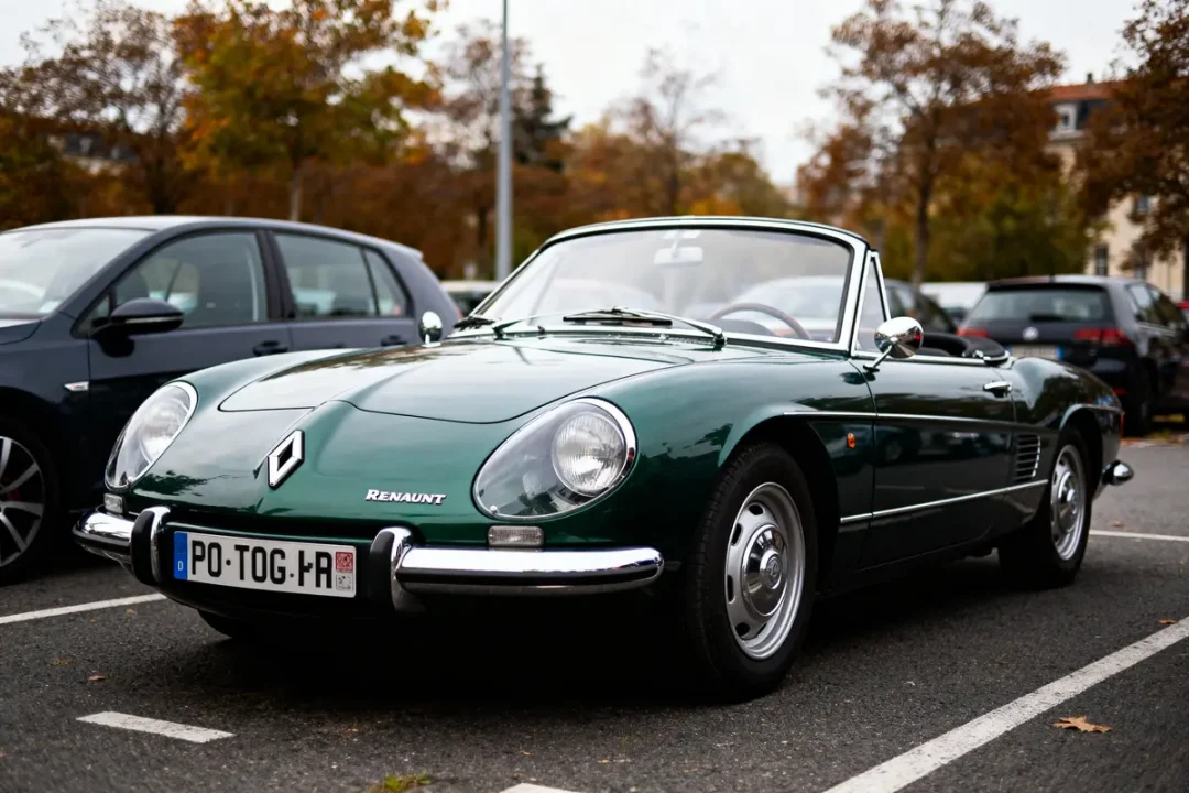 Voiture de collection Renault décapotable verte stationnée sur un parking, entourée d'autres véhicules.