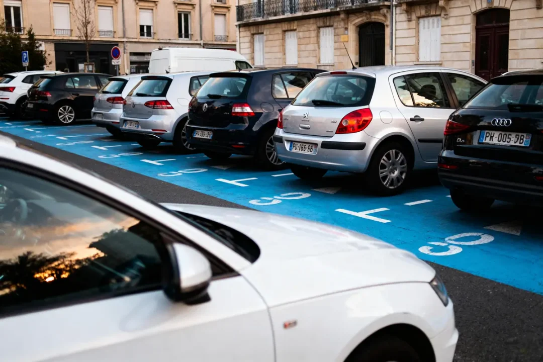 Plusieurs voitures garées sur une aire de stationnement bleue en ville, bâtiments en arrière-plan.