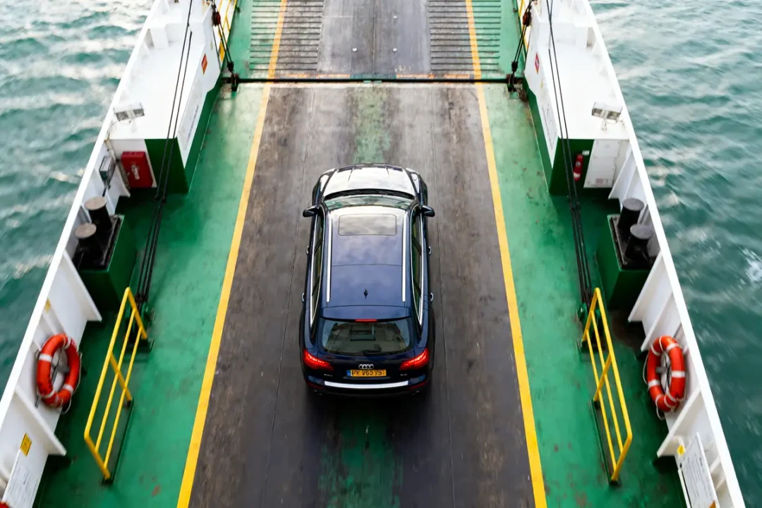 Voiture noire sur un ferry en mer, entourée de bordures vertes et blanches.