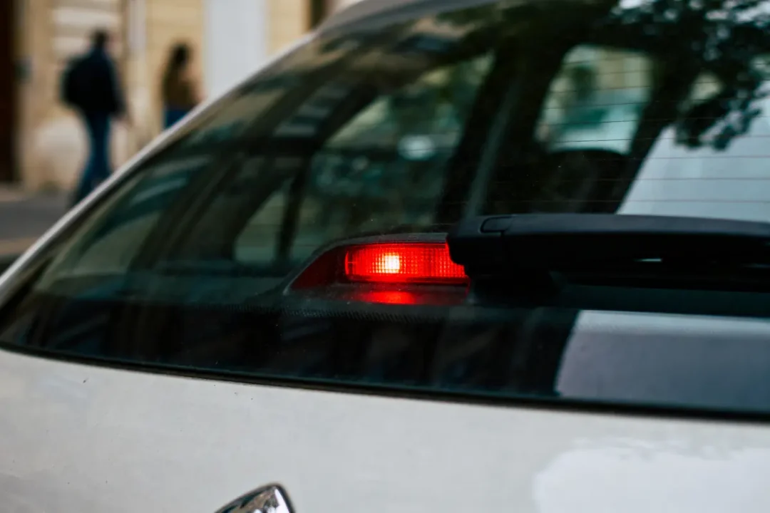Feu stop rouge allumé à l'arrière d'une voiture, essuie-glace visible sur la vitre arrière.