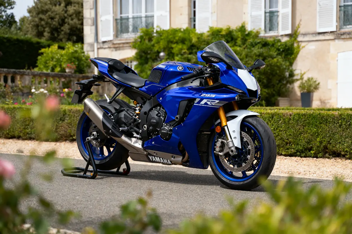 Moto sportive Yamaha R1 bleue stationnée devant un bâtiment élégant, entourée de verdure.